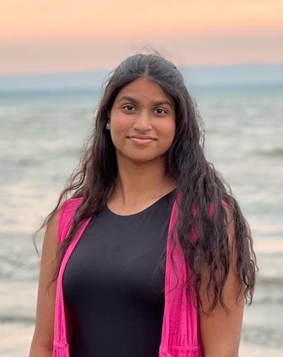 A photo of Trisha. She is a young Southeast Asian woman and is smiling, set against a water background.
